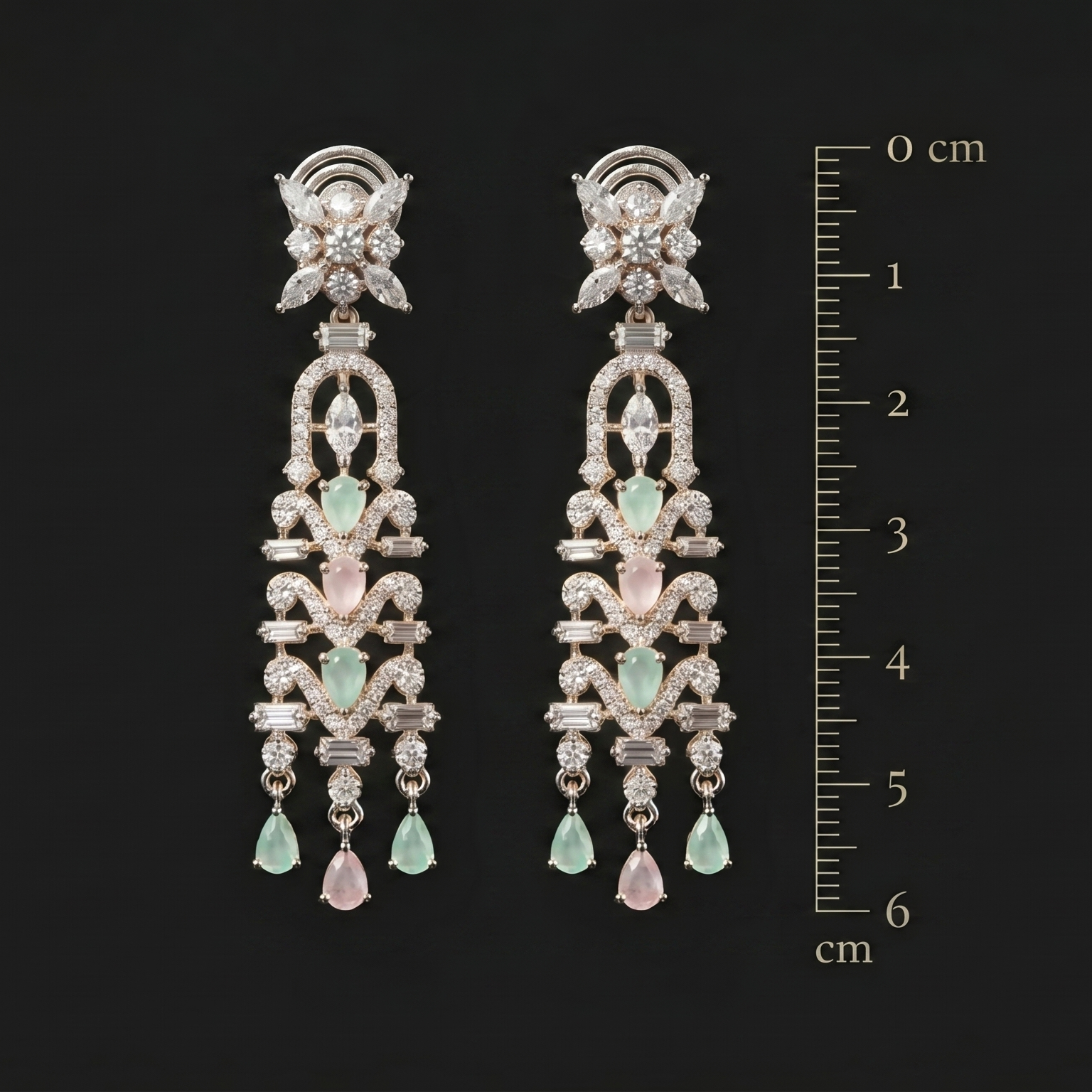 Pair of elegant earrings with green gemstones and a ruler for scale on a black background