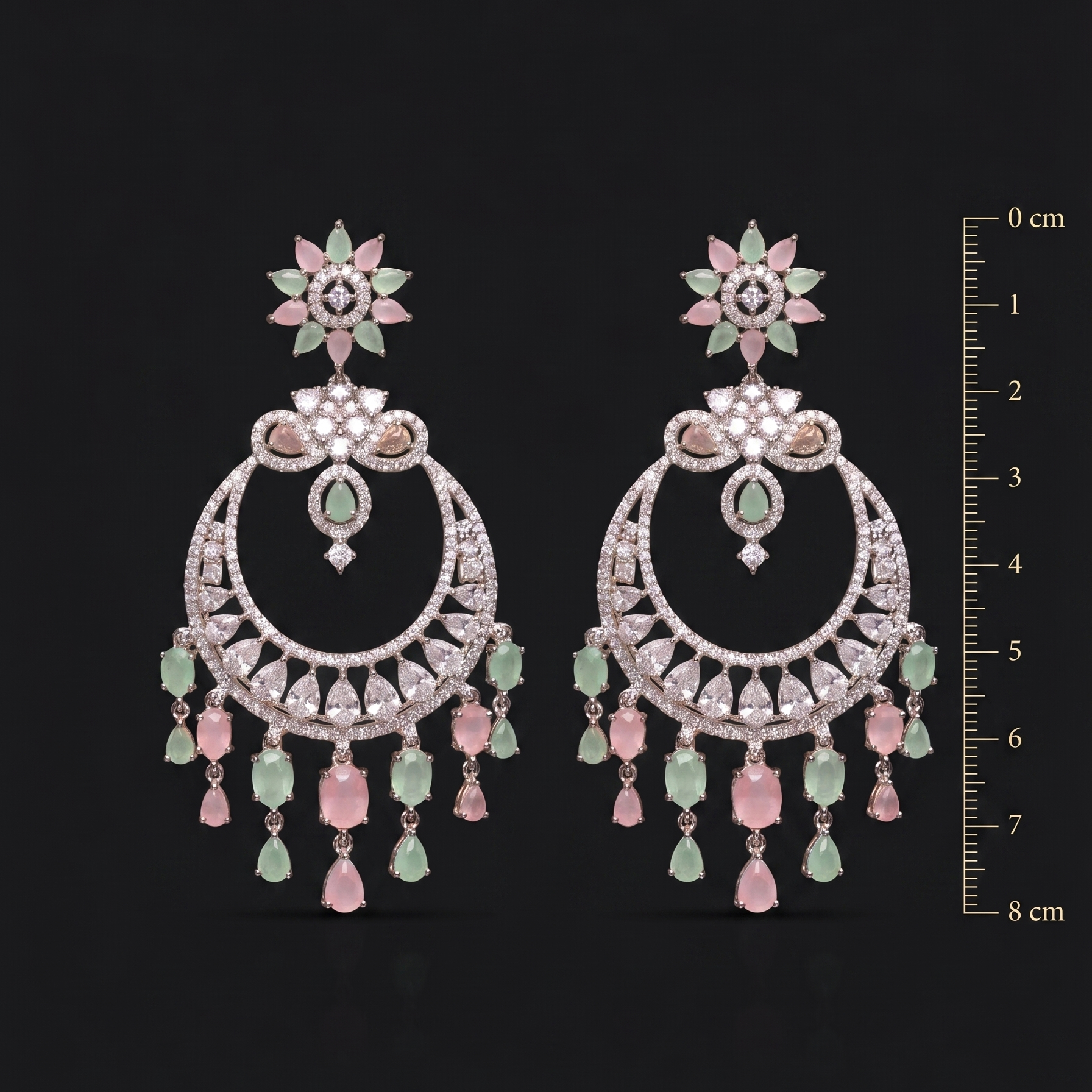 Pair of ornate earrings with gemstones on a black background, accompanied by a measurement scale.