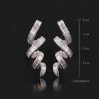 Pair of silver earrings with clear stones on a black background with measurement scale.