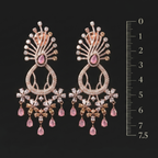 Pair of ornate earrings with pink gemstones and a scale for size reference on a black background.