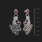 Pair of ornate earrings with gemstones on a black background with a measurement scale.
