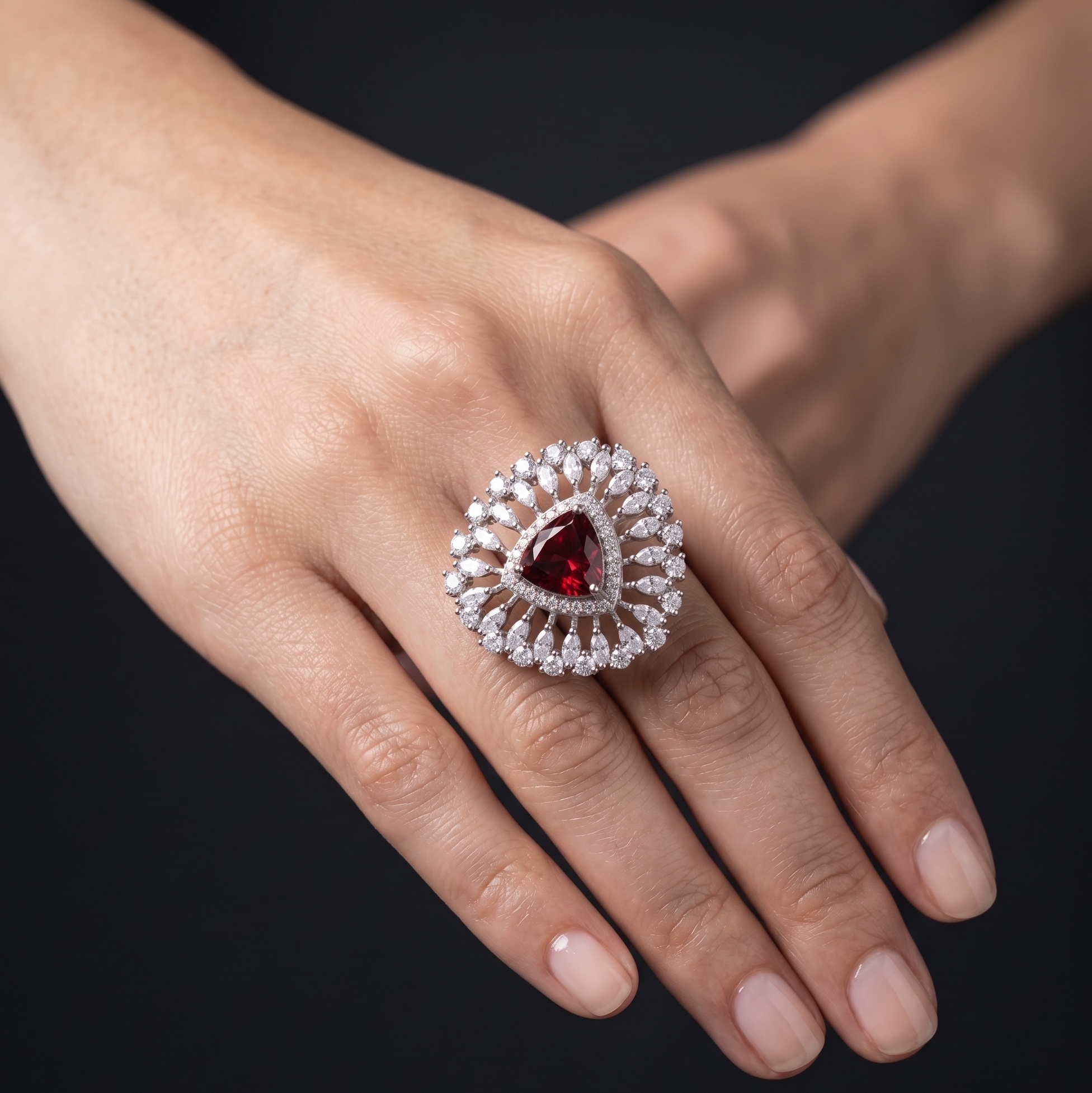 Hand wearing a decorative ring with a red gemstone on a black background
