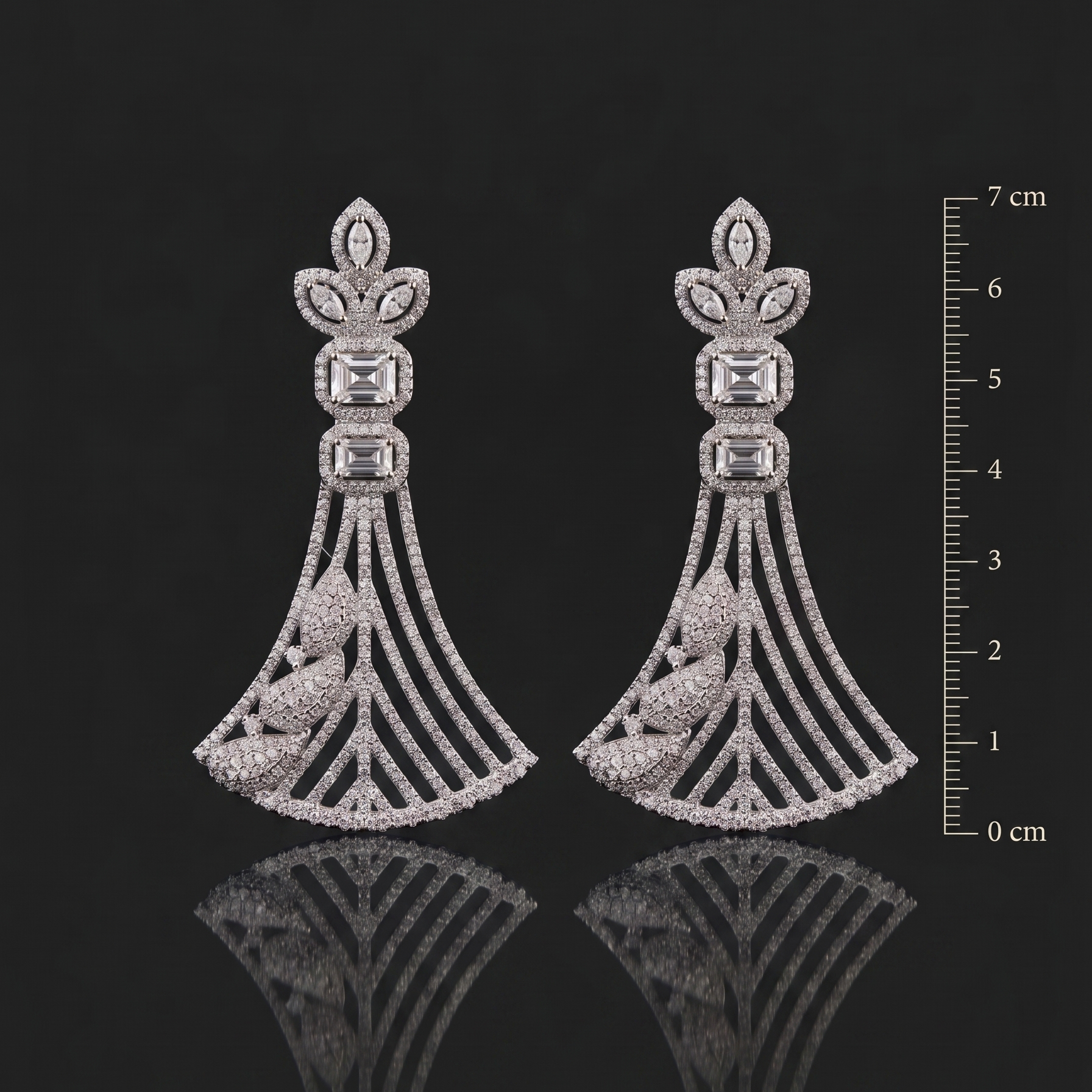 Pair of ornate silver earrings with gemstones on a black background with a scale for size reference.