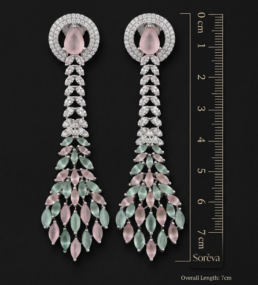 Pair of long, elegant earrings with gemstones and a ruler for scale on a dark background.