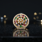 Gold ring with colorful gemstones on a reflective surface with blurred lights in the background