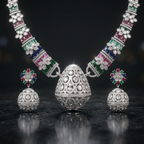 Jewelry set with necklaces, earrings, and a pendant on a reflective surface with blurred lights in the background.