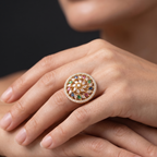 Close-up of a hand wearing a decorative ring with gemstones on a neutral background