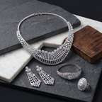 Silver jewelry set including necklace, earrings, bracelet, and ring on a dark surface.
