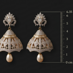 Pair of ornate earrings with a measurement scale on a black background