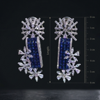 Pair of silver earrings with blue and clear gemstones, shown with a measurement scale on a black background.
