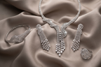 Silver jewelry set including necklace, earrings, and bracelet on a beige fabric background
