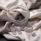 Silver jewelry set including necklace, earrings, and ring on a beige fabric background