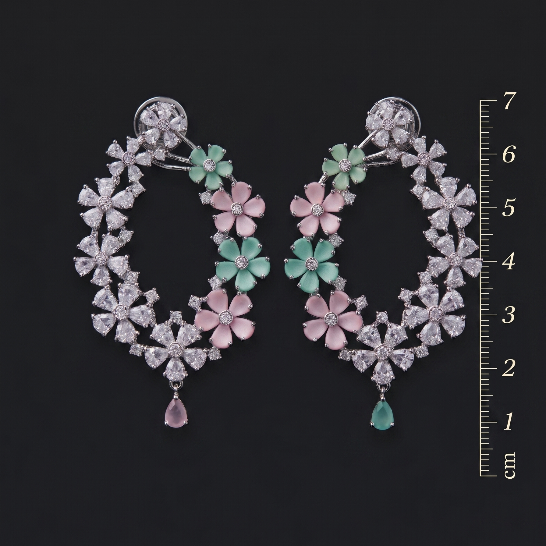 Pair of floral earrings with gemstones on a black background, accompanied by a ruler for scale.