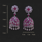 Pair of ornate earrings with gemstones on a dark background with measurement scale.