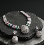 Silver necklace and earrings with colorful gemstones on a dark stone surface