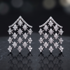 Pair of diamond earrings on a dark reflective surface with a blurred background