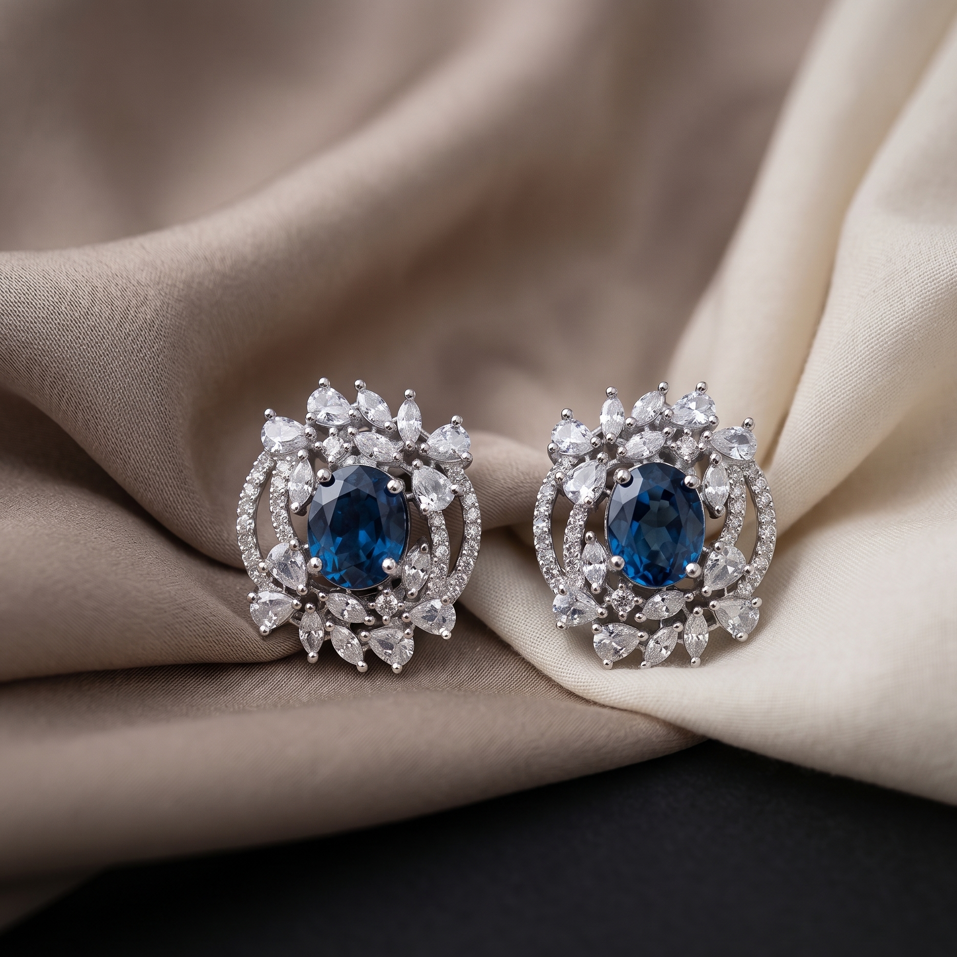 Pair of earrings with blue gemstones and diamond-like stones on a beige fabric background