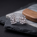 Pair of diamond earrings on a dark stone surface with a wooden block in the background