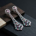 Pair of elegant earrings with pink and green gemstones on a dark surface