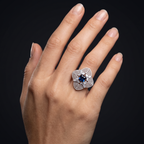 Hand wearing a decorative ring with a blue gemstone on a black background