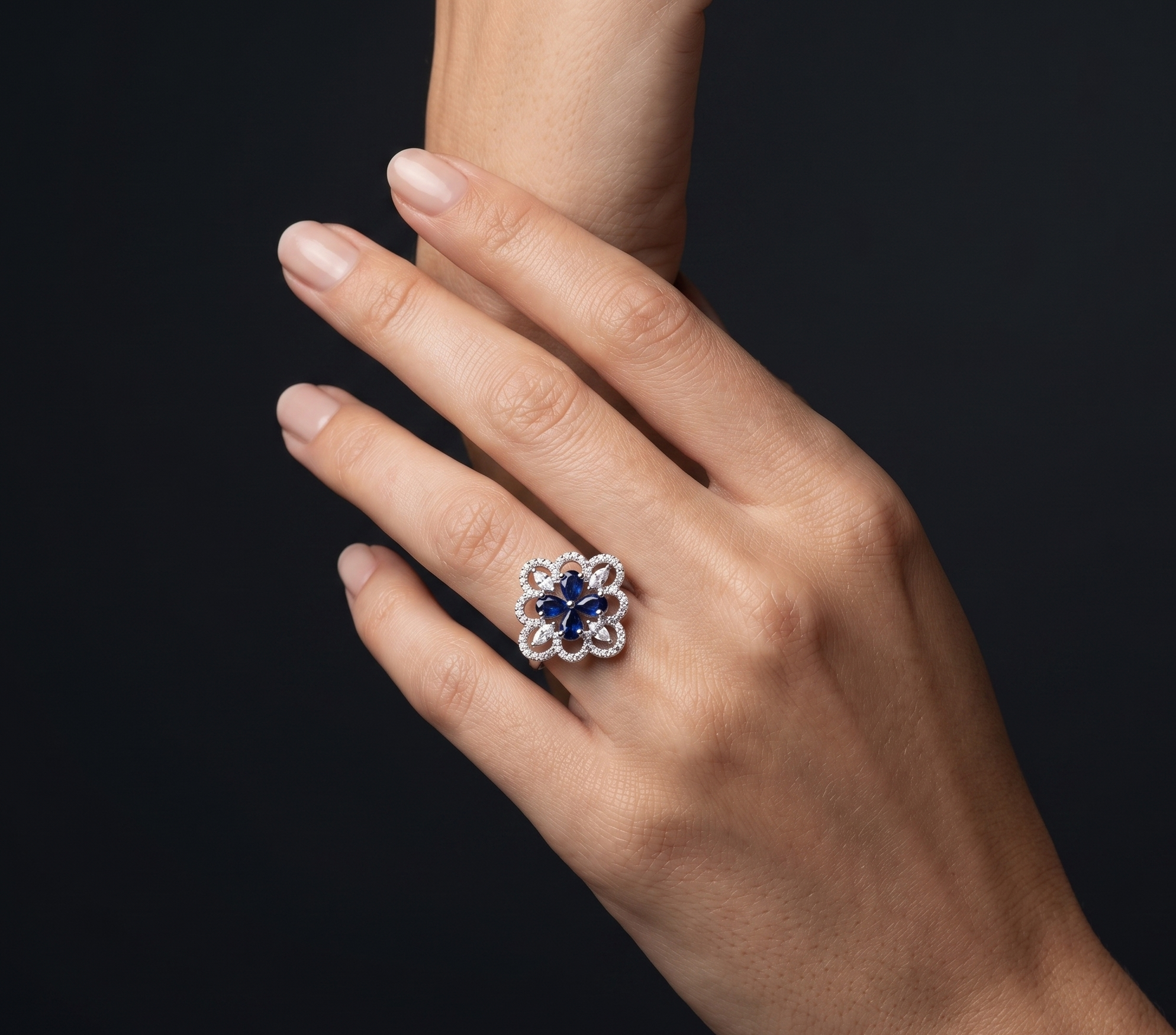 Hand wearing a ring with a blue gemstone on a black background