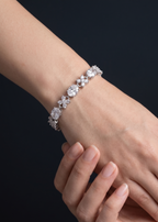 Close-up of a hand wearing a silver bracelet with clear stones on a dark background
