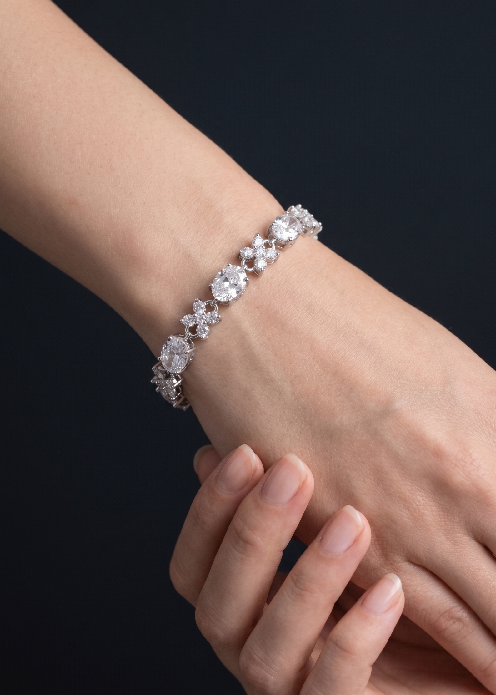 Close-up of a hand wearing a silver bracelet with clear stones on a dark background
