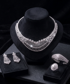 Silver jewelry set including necklace, earrings, and ring on a black stand with a dark background.