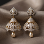 Pair of ornate earrings with pearl drops on a textured fabric background