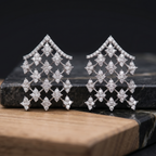 Pair of diamond earrings on a dark stone surface with a wooden base